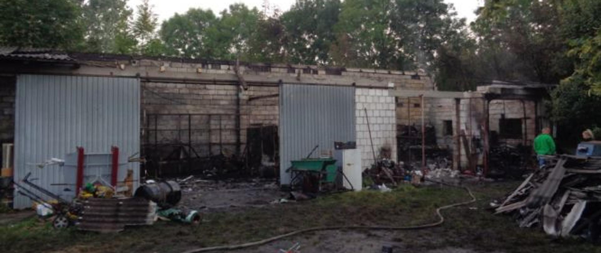 Zdjęcie przedstawia spalone wnętrze garażu murowanego. Przed budynkiem znajdują nadpalone elementy garażu. 