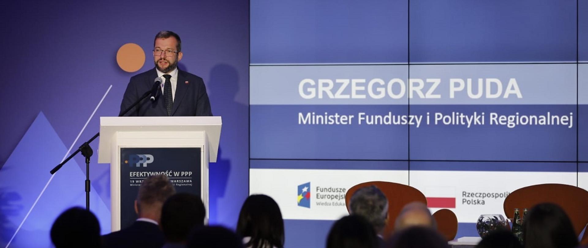 Minister Grzegorz Puda stoi przy mównicy i przemawia do mikrofonu, po jego prawej stronie grafika informująca, że przemawia szef MFiPR
