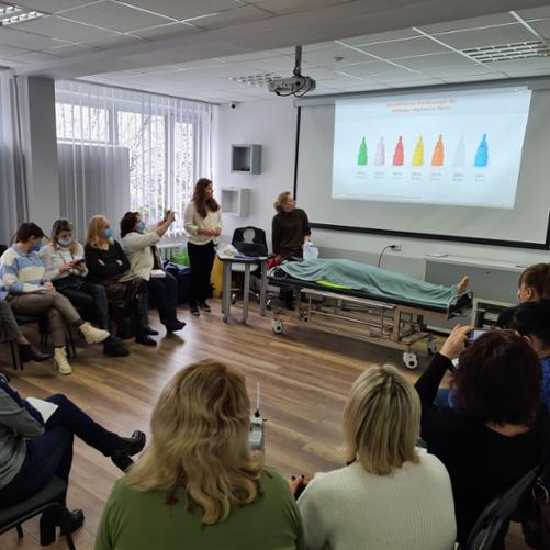 Kobiety siedzą w kręgu, obserwują prowadzącą, ekran i fantoma ratowniczego.