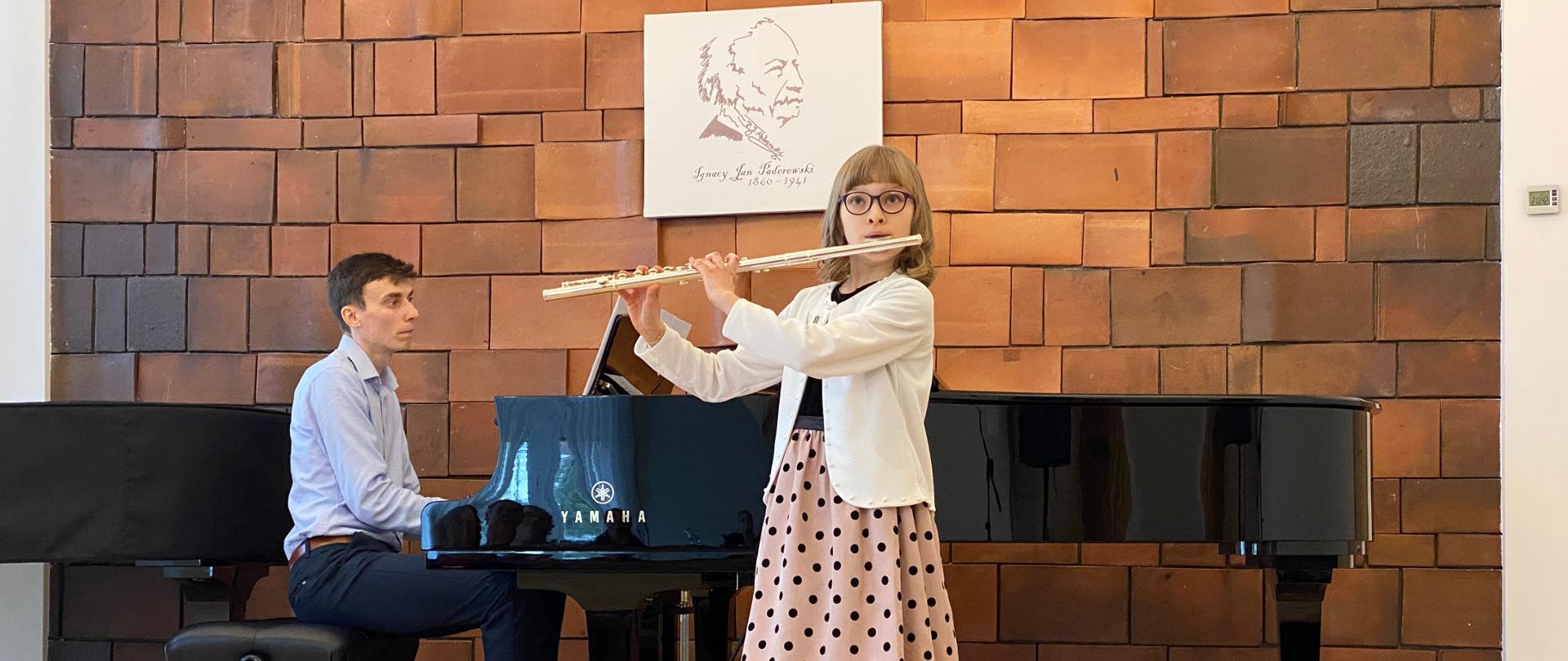 Dziewczynka gra na flecie. Akompaniuje jej pianista.