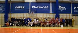 Wszyscy zebrani na hali GOSiR podczas zawodów na wspólnym, grupowy zdjęciu. W tle na ścianie napisy w oknach "netex, mazowsze"