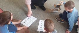 Inspektor Oddziału pokazująca dzieciom kartki z rycinami owadów oraz drewniany domek dla owadów.