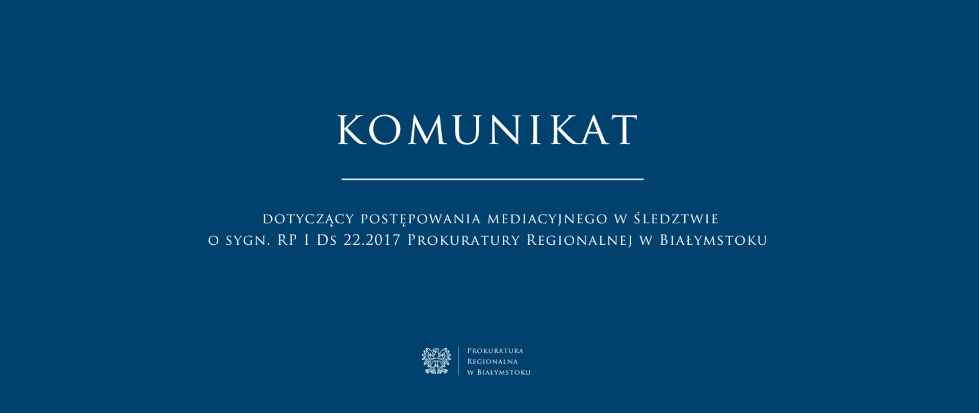 Grafika informacyjna przedstawia białe napisy umieszczone na jednolitym, ciemnoniebieskim tle. W centrum znajduje się duży nagłówek „KOMUNIKAT”, pod którym widnieje cienka pozioma linia oraz tekst dotyczący sygnatury sprawy. Na samym dole, na środku, umieszczone zostało oficjalne logo Prokuratury Regionalnej w Białymstoku wraz z godłem Polski.