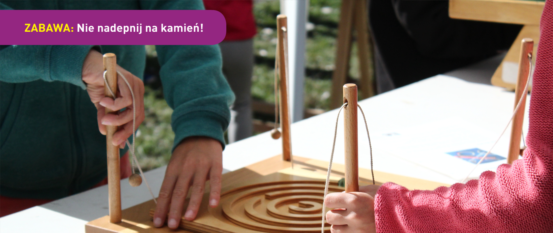 Na zdjęciu widać dzieci bawiące się grą złożoną z planszy, patyczków i rzemienia. U dołu znajduje się pasek logotypów: Europejskie Fundusze Polska Cyfrowa, Ministerstwo Cyfryzacji, NASK i Unia Europejska Europejski Fundusz Rozwoju Regionalnego.