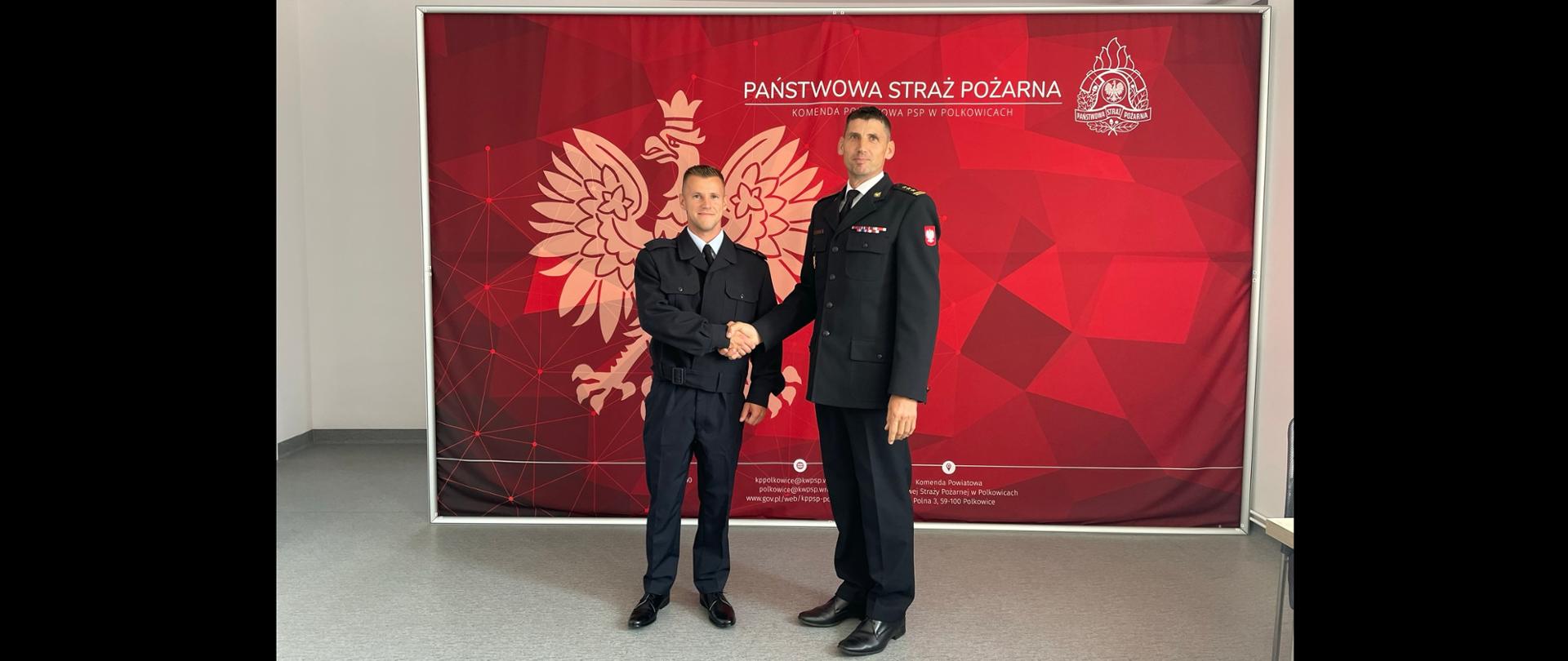 Komendant Powiatowy PSP w Polkowicach oraz Nowozatrudniony Strażak na tle logo z PSP