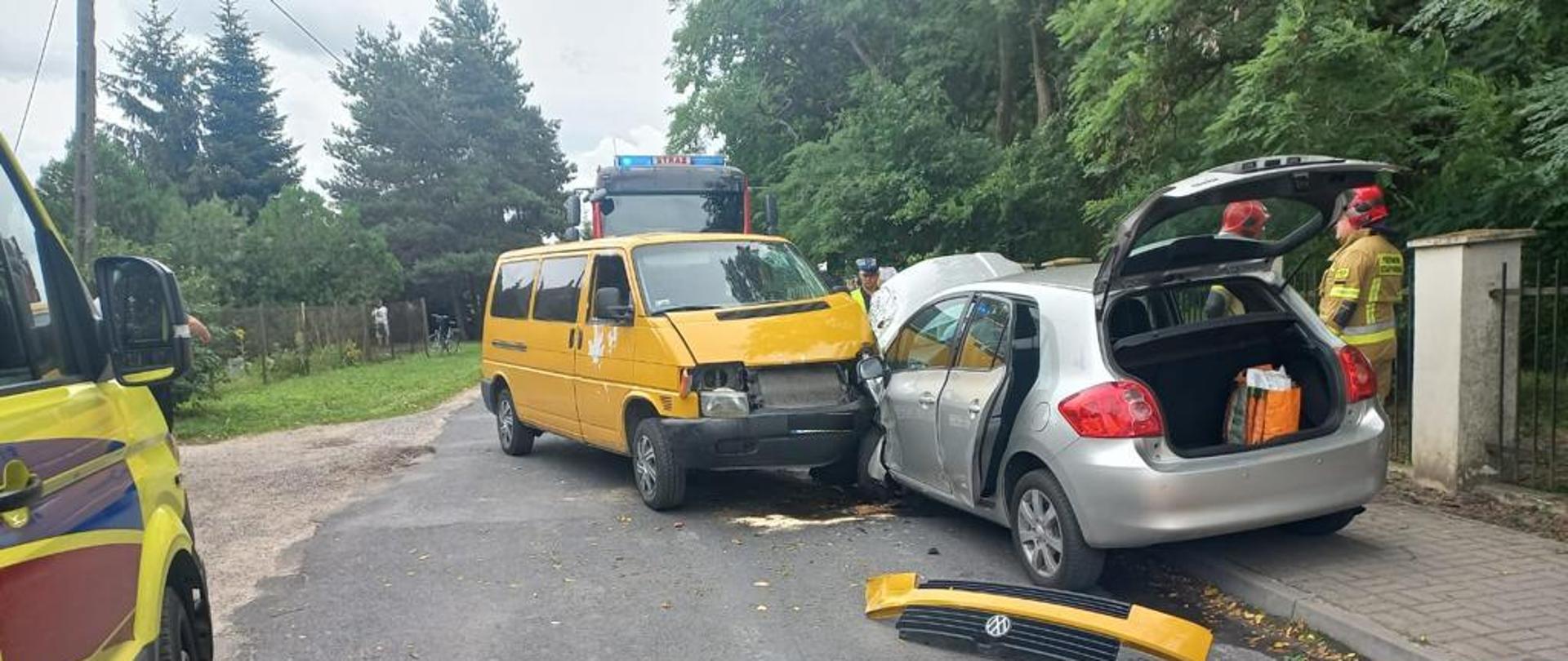 Na zdjęciu znajdują się samochody osobowe po wcześniejszym zderzeniu. Po lewej stronie znajduje się Zespół Ratownictwa Medycznego, po prawej stronie znajduje się samochód policyjny. Dalej widać samochody osobowe po wcześniejszym zderzeniu, za samochodem z prawej strony znajdują się strażacy, z tyłu między samochodami znajduje się policjant, z tyłu za samochodami znajduje się wóz strażacki.