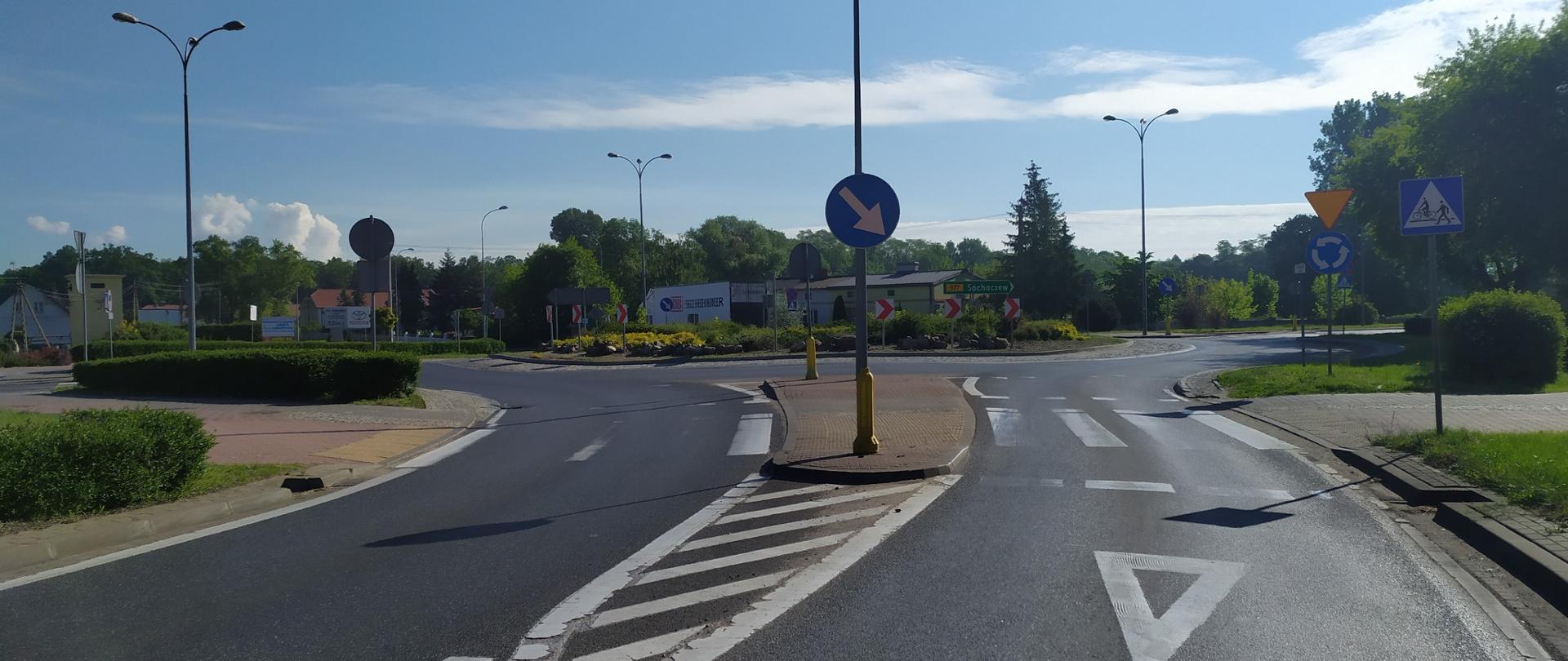 Na zdjęciu widoczne rondo w wyspą zieleni na środku. Słoneczna pogoda, niebieskie niebo z niewielkim zachmurzeniem