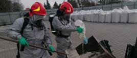 Zdjęcie przedstawia działania gaśnicze podczas pożaru hali magazynowej. Strażacy w ubraniach specjalnych chroniących przed czynnikami chemicznymi oraz sprzęcie ODO realizują działania gaśnicze