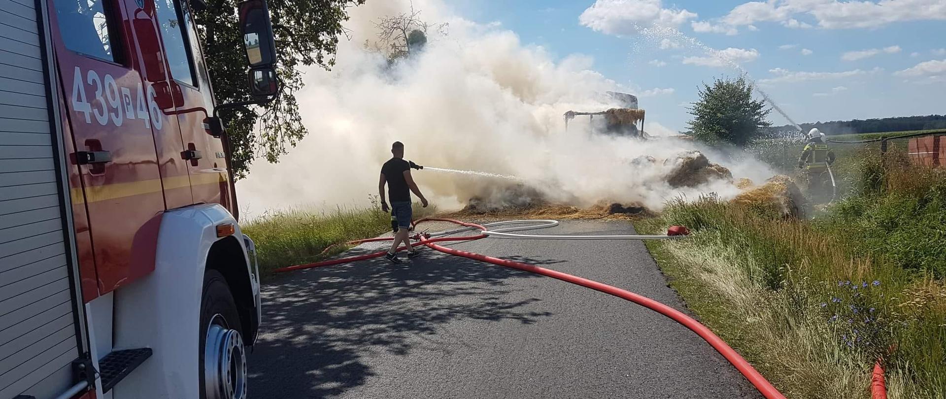Strażacy gaszą baloty na przyczepie.