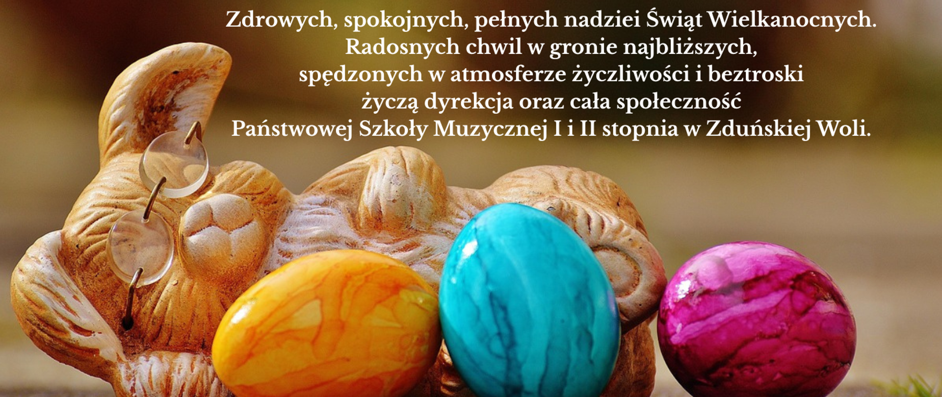 na beżowym tle trzy kolorowe jaja, a za nimi leżąca figurka zająca w okularach. nad nimi napis Zdrowych, spokojnych, pełnych nadziei Świąt Wielkanocnych. Radosnych chwil w gronie najbliższych, spędzonych w atmosferze życzliwości i beztroski życzą dyrekcja oraz cała społeczność Państwowej Szkoły Muzycznej I i II stopnia w Zduńskiej Woli.