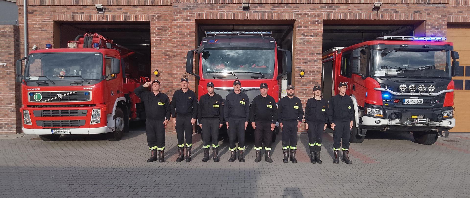 Na zdjęciu zmiana I pełniąca służbę w Jednostce Ratowniczo Gaśniczej w Pucku oddaje hołd tragicznie zmarłym strażakom z Poznania. Funkcjonariusze ustawieni są w szeregu. Ubrani są w ubrania koszarowe. Na drugim planie wozy strażackie.