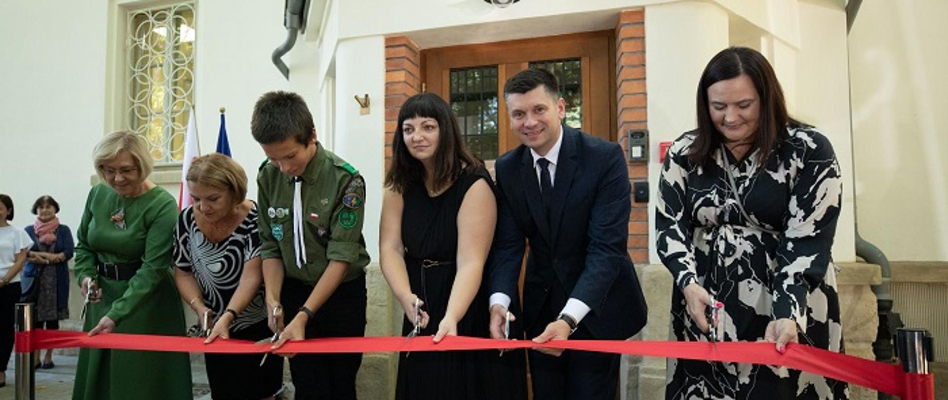 6 osób przecina czerwoną wstęgę otwierając Centrum Zdrowia Psychicznego dla Dzieci i Młodzieży w Krakowie. Wśród tych osób jest wiceminister Małgorzata Jarosińska-Jedynak, wojewoda woj. małopolskiego oraz p.o. Dyrektora Szpitala: dr n. med. Anna Depukat