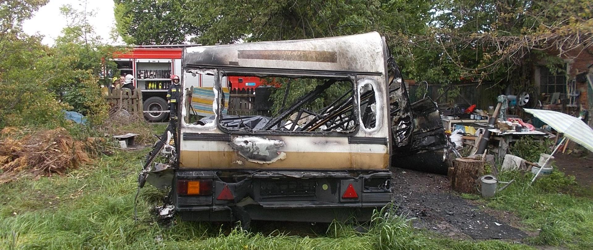 Zgliszcza po przyczepie kempingowej, w tle samochód pożarniczy
