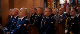 Funkcjonariusze służb mundurowych oraz zaproszeni goście siedzą w ławkach w kościele.