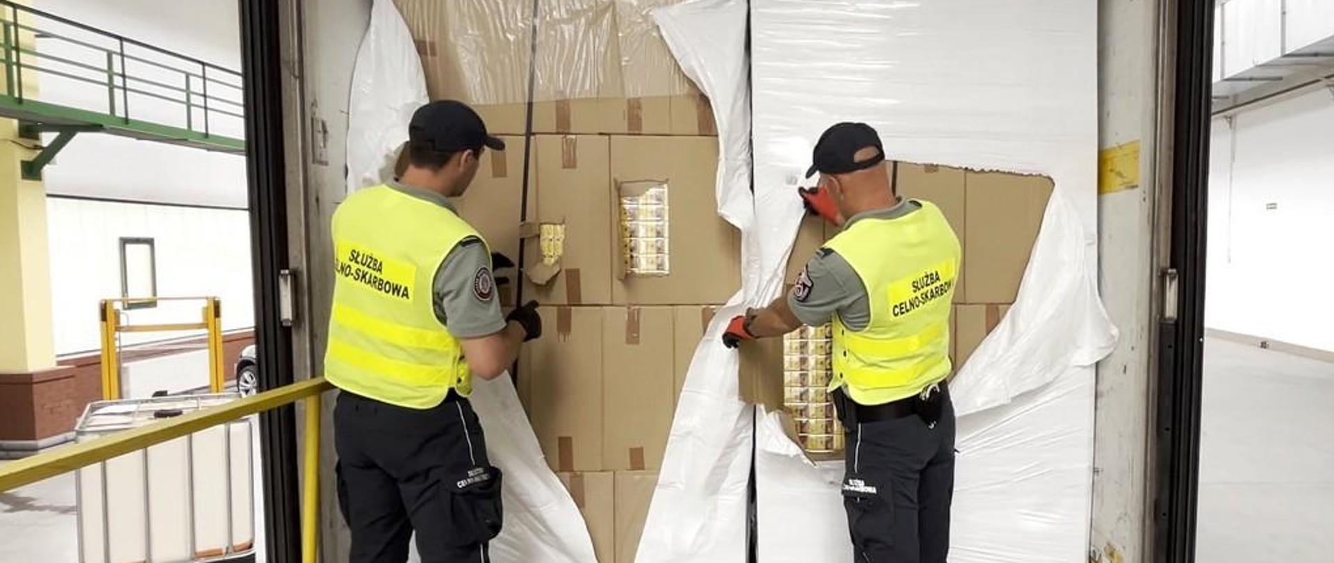 Funkcjonariusze Służby Celno-Skarbowej podczas sprawdzania kartonów z papierosami, na naczepie.