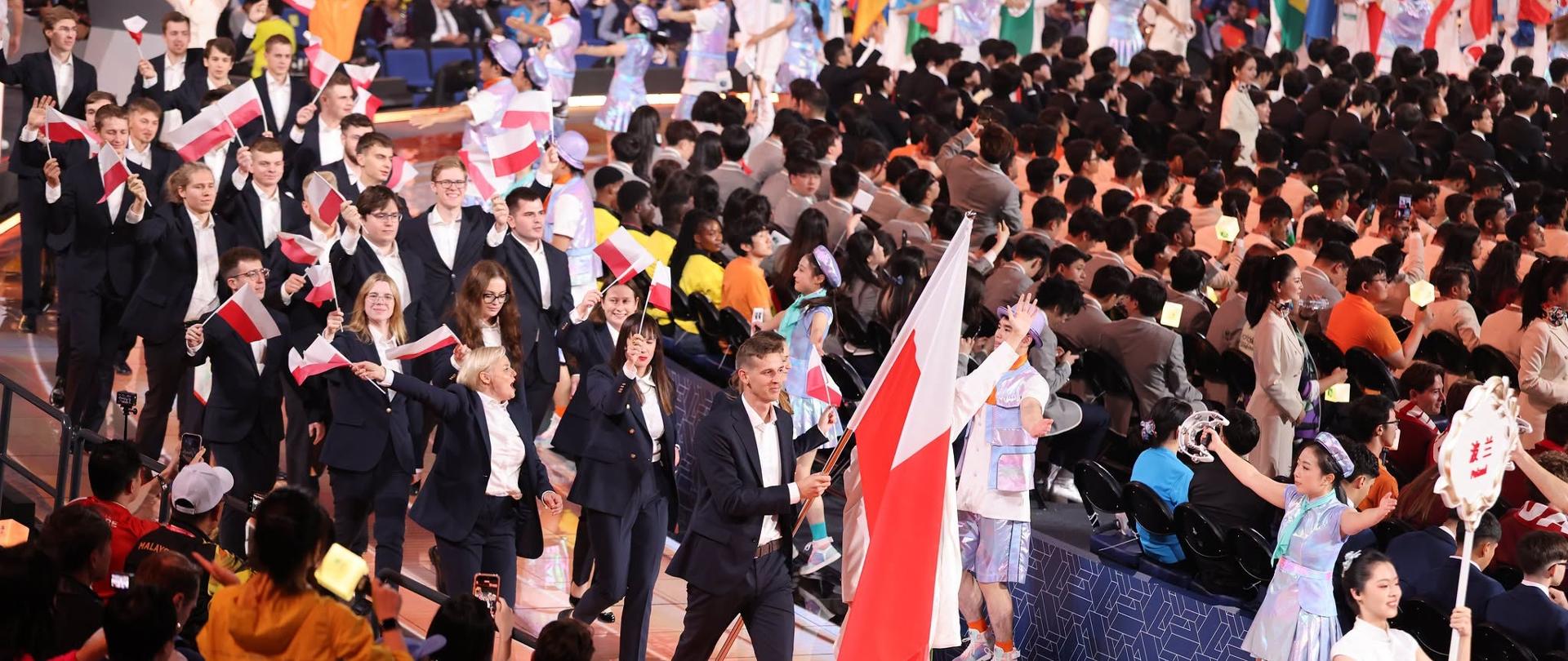 Ceremonia otwarcia zawodów WorldSkills. Polska ekipa w garniturach przechodzi, machając flagami.