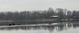 Na zdjęciu widoczny akwen wodny. Na wodzie trzech strażaków - dwóch z lewej strony zdjęcia, trzeci holowany liną widoczny po prawej stronie zdjęcia
