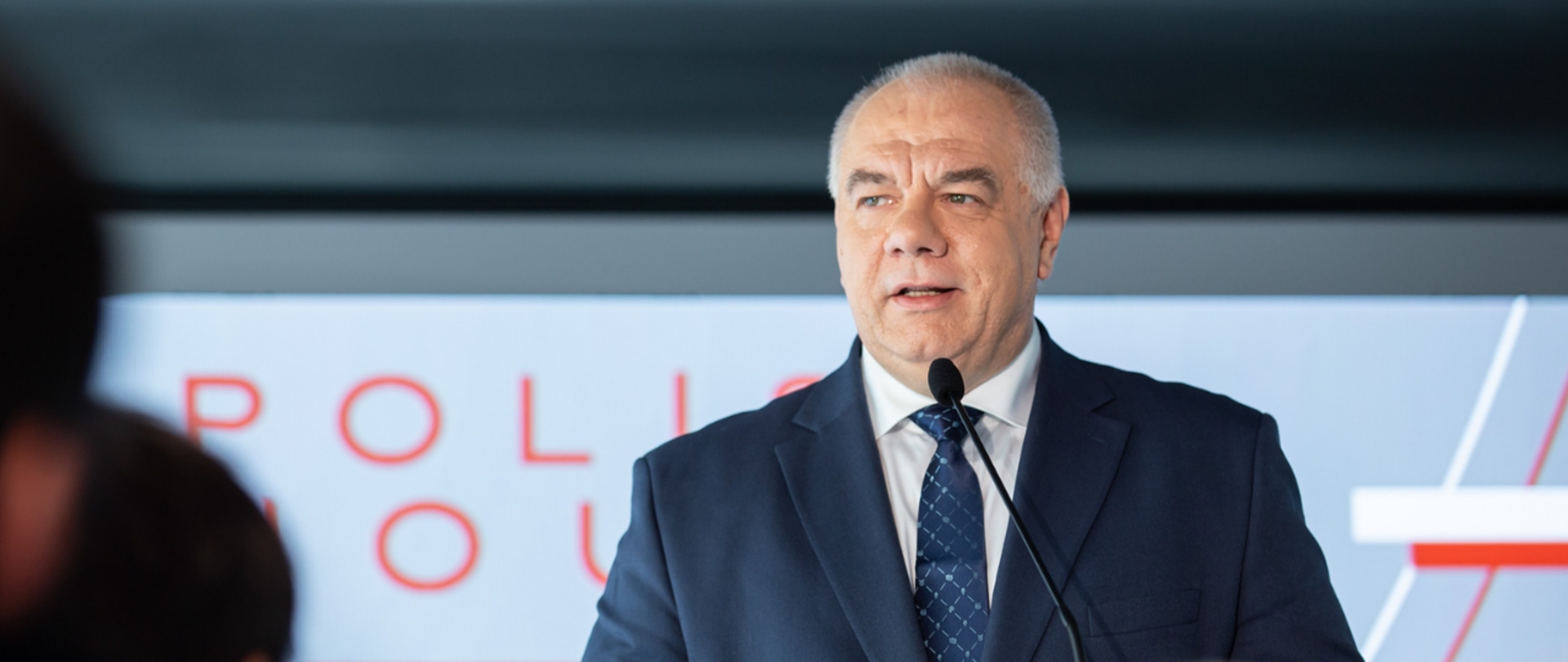 Wicepremier Jacek Sasin stoi za mównicą. W tle ścianka.
