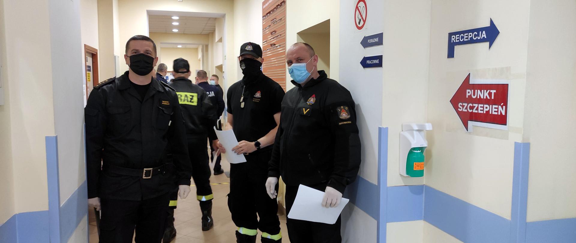 Funkcjonariusze Państwowej Straży Pożarnej w korytarzu oczekując na szczepienie.