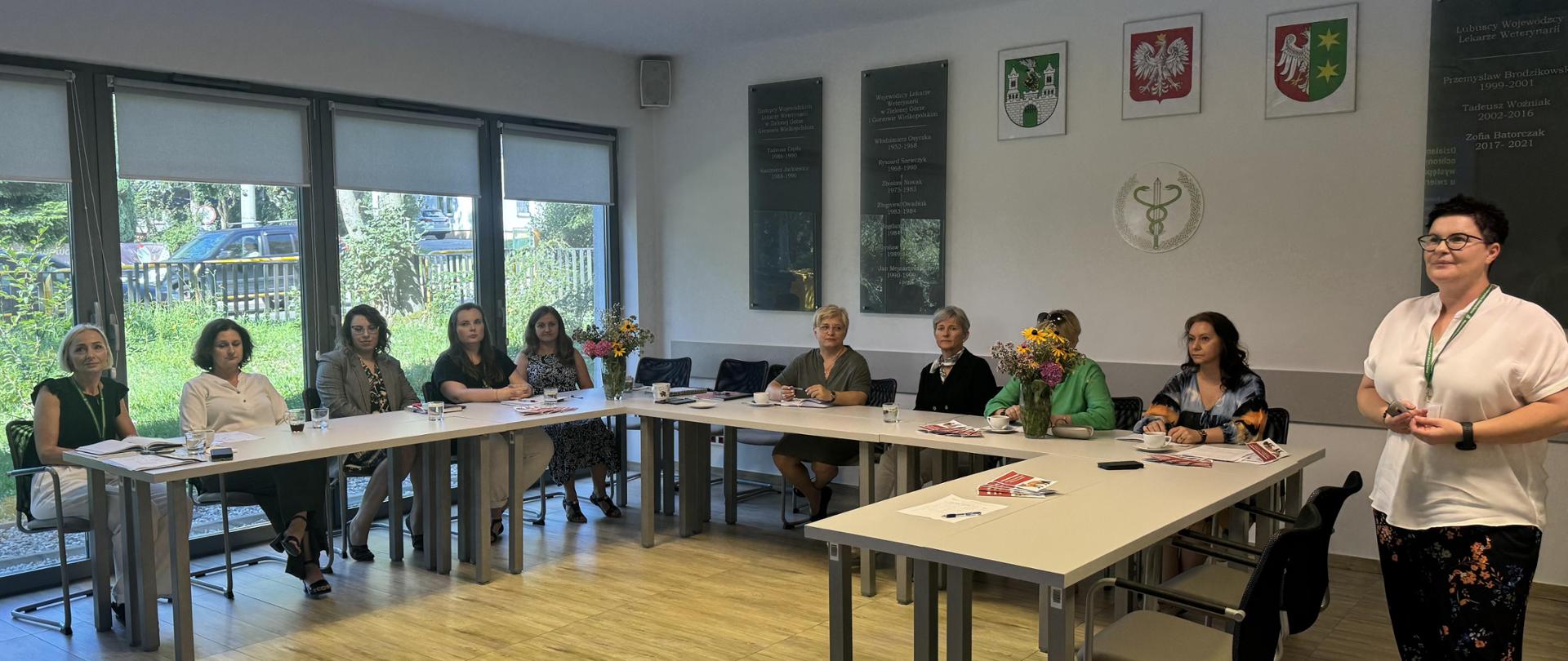 Przy stole siedzą uczestnicy spotkania w Wojewódzkim Inspektoracie Weterynarii w Zielonej Górze, obok stoi jedna osoba