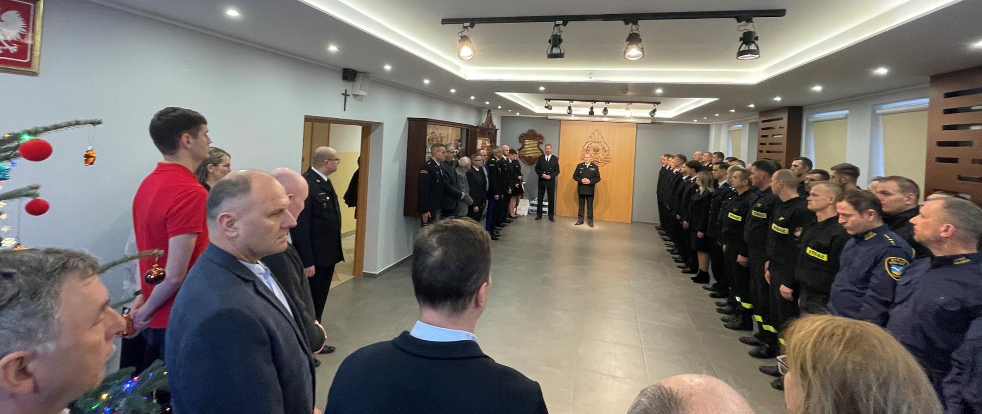 Świetlica komendy. Do okoła sali ustawieni strażacy, strażnicy miejscy oraz zaproszeni goście