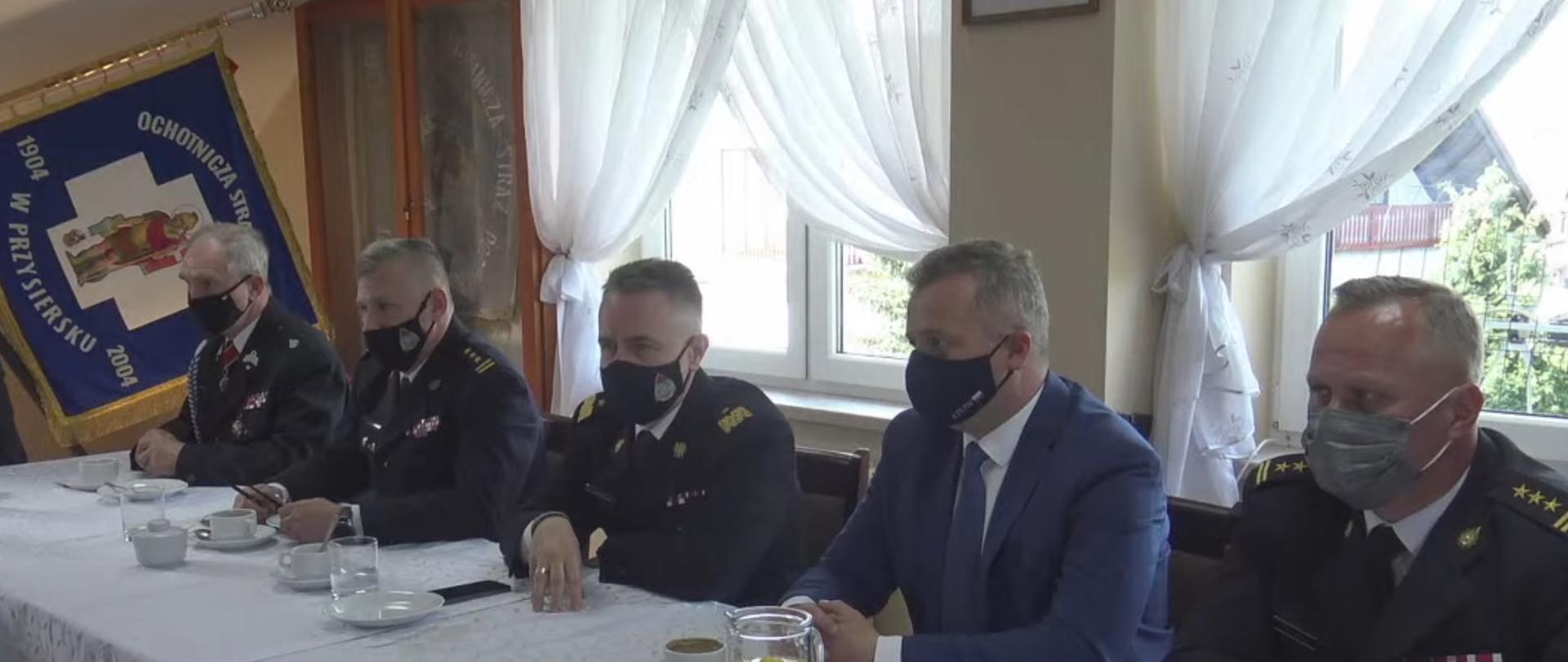 Konsultacje społeczne projektu ustawy o OSP. Pięciu mężczyzn siedzących przy stole. Pośrodku komendant główny PSP nadbryg. Andrzej Bartkowiak. W tle (po lewej stronie) sztandar Ochotniczej Straży Pożarnej w Przysiersku