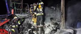 Jest noc, widać strażaków jak gaszą pożar opon i kombajn