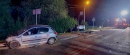 Samochody osobowe po zderzeniu znajdują się na poboczu drogi. Na drugim planie samochód strażacki.