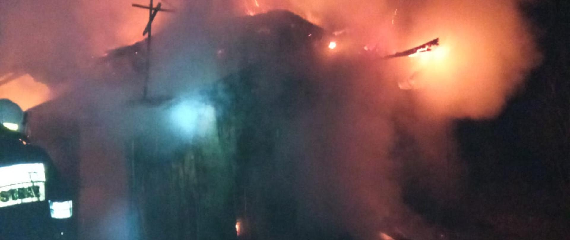 Budynek mieszkalny (pustostan) w ogniu. Strażak po lewej prowadzi działania gaśnicze