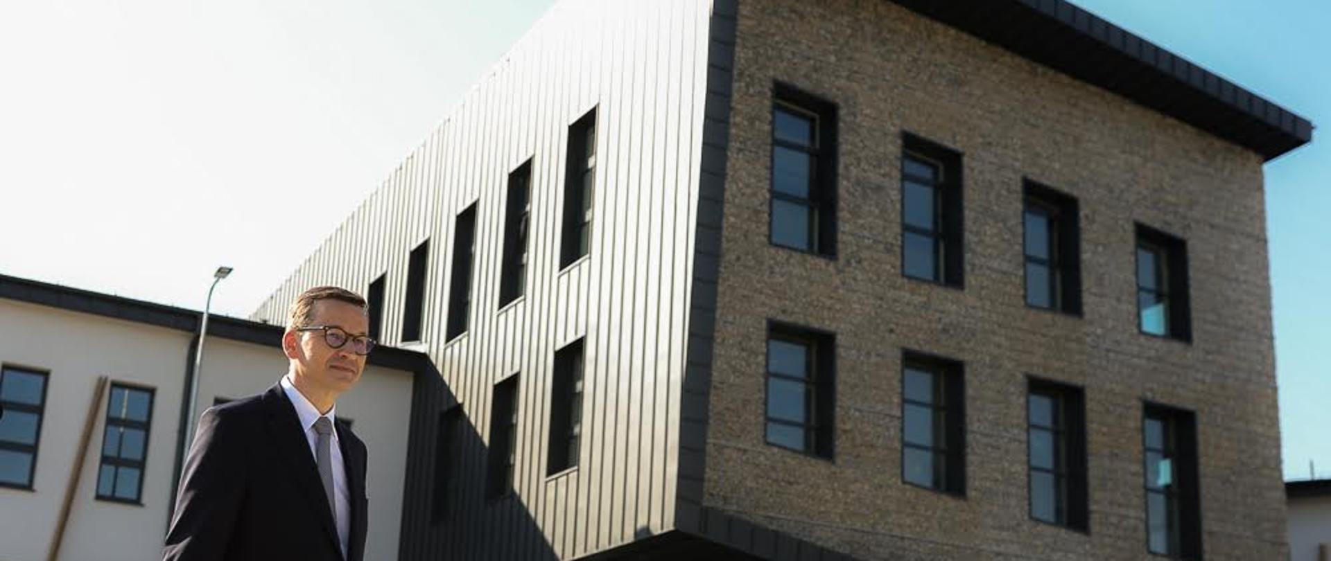 Premier Mateusz Morawiecki stoi przed nowoczesnym budynkiem szkoły.