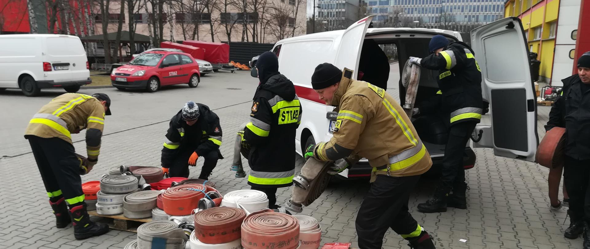 Strażacy wypakowują węże strażackie z busa Komendy Powiatowej PSP w Żyrardowie.