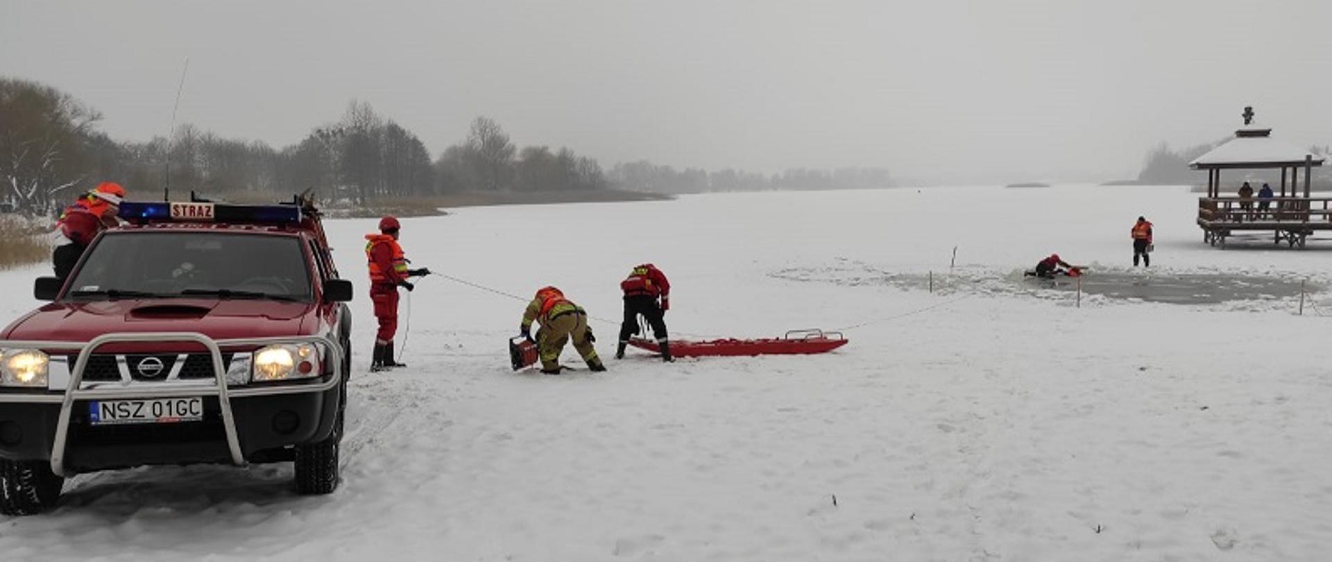 Zdjęcia przedstawia ratowników przygotowujących się do transportu poszkodowanego przy pomocy deski lodowej