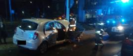 Zdjęcie w porze nocnej. Widać uszkodzony pojazd. Oświetlenie sztuczne. Na zdjęciu widać pojazd ratowniczo-gaśniczy z sygnalizacją ostrzegawczą, niebieską.