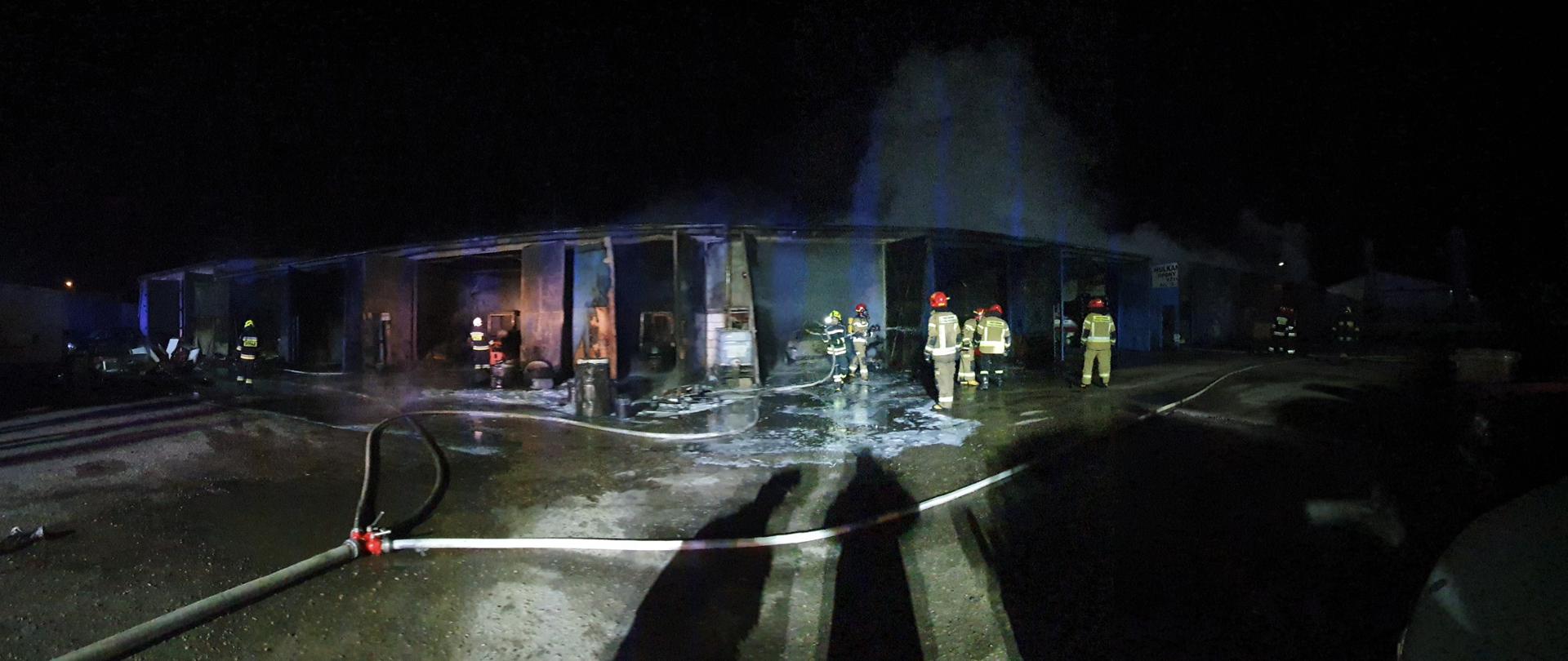 Na zdjęciu widoczny spalony budynek, w tle pracujący strażacy