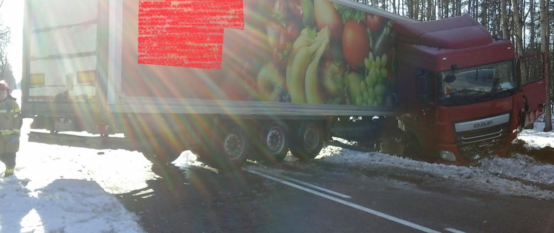 Samochód ciężarowy po wypadku. Ciągnik siodłowy stoi w przydrożnym rowie, naczepa blokuje całą szerokość jezdni.