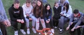 Grupa uczniów piekących kiełbaski w ognisku