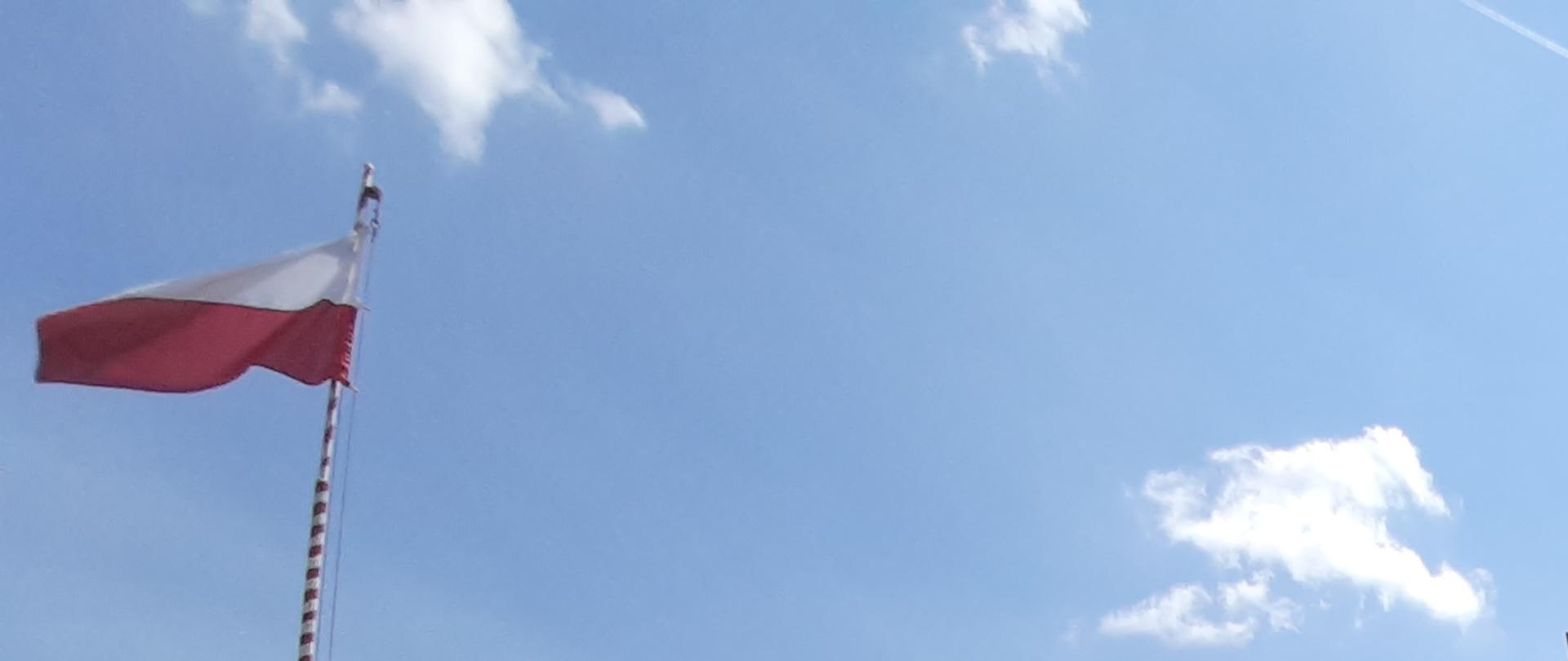 Biało czerwona flaga na maszcie i obok budynek straży pożarnej