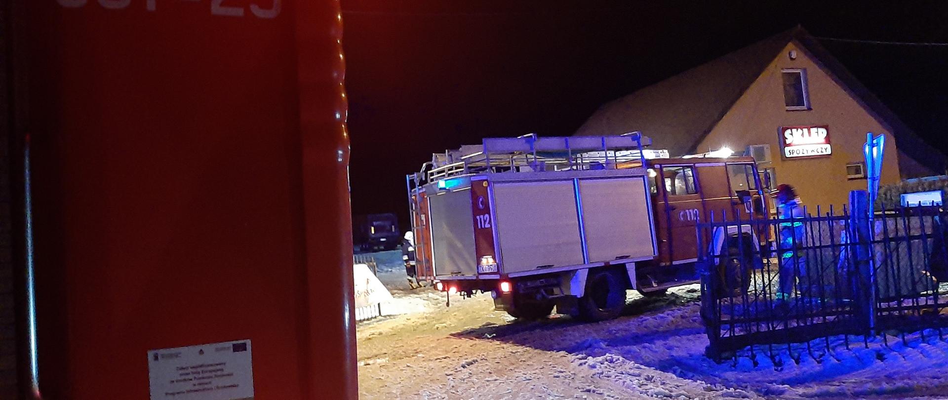 Na zdjęciu widzimy dwa samochody pożarnicze biorące udział w akcji ratowniczo-gaśniczej w miejscowości Piotrów-Gułaczów. W tle sklep spożywczy, w którym doszło do zapalenia się sadzy w przewodzie dymowym.