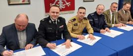 Na zdjęciu w sali konferencyjnej Komendy Powiatowej Policji w Gorlicach widoczni przedstawiciele służb mundurowych i instytucji z powiatu gorlickiego przy stole podpisujący apel służb powiatu gorlickiego dotyczący niewypalania traw. 