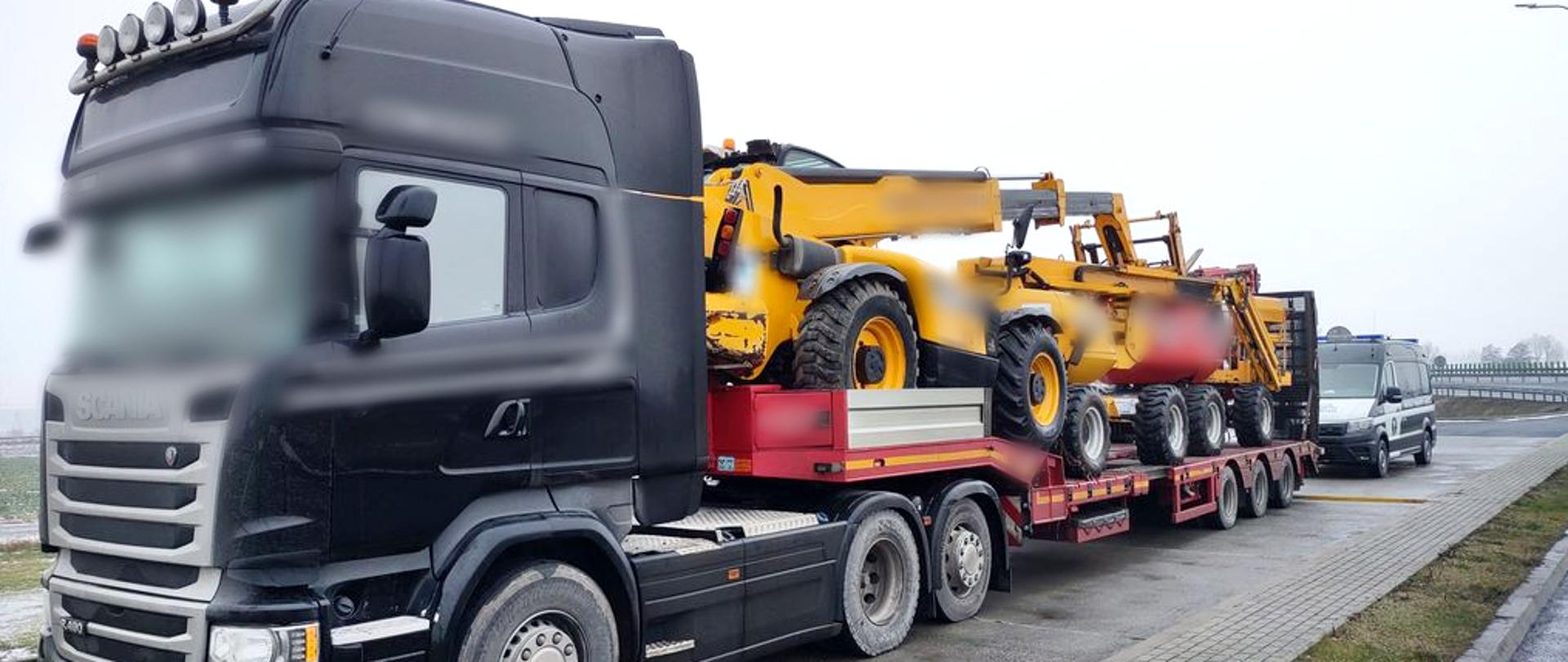 Na pierwszym planie ciągnik siodłowy koloru czarnego z naczepą (platformą przeznaczoną do transportu maszyn) zatrzymany do kontroli na S5. Na platformie znajdują się trzy maszyny. W oddali radiowóz ITD.