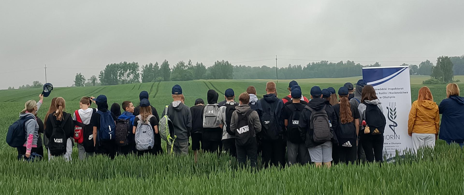 Grupa młodych ludzi stoi na tle zielonej roślinności przy banerze z napisem PIORiN