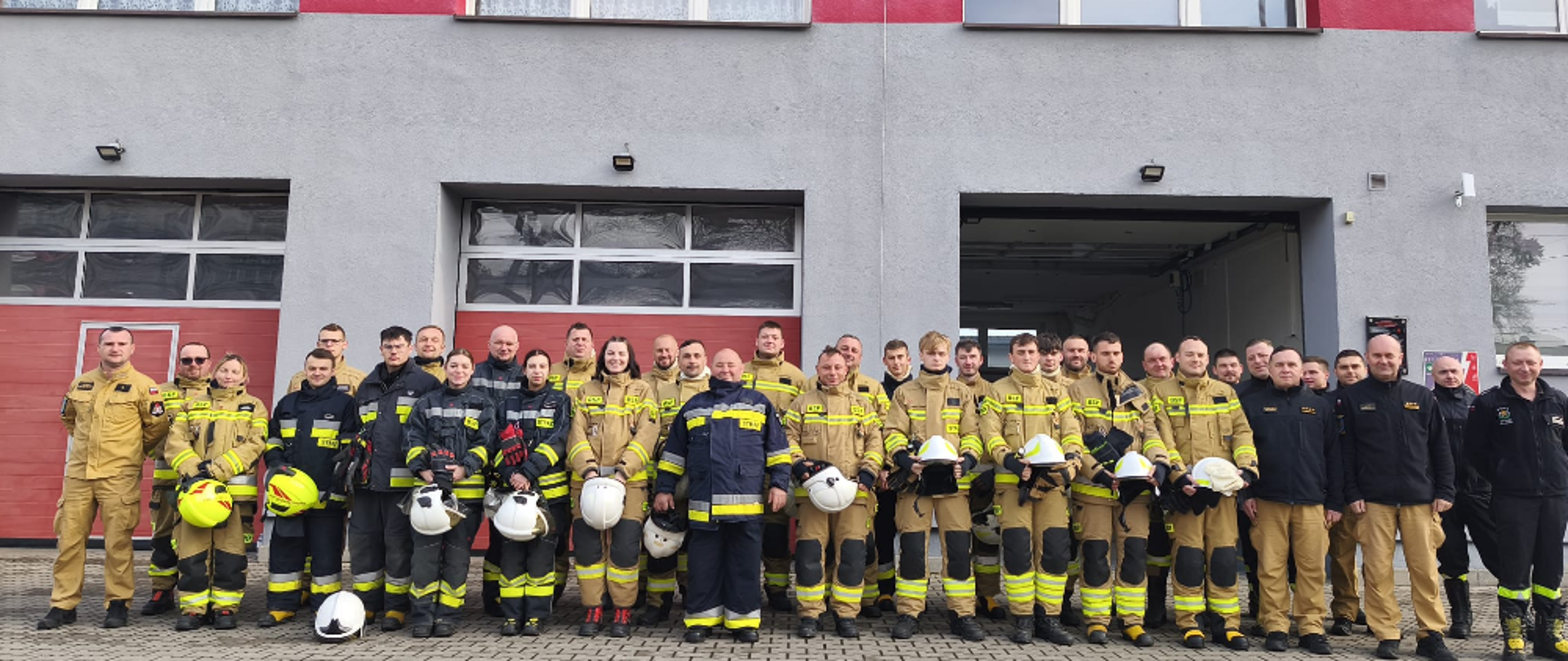 Zdjęcie przedstawia grupę strażaków w mundurach stojących przed budynkiem remizy OSP