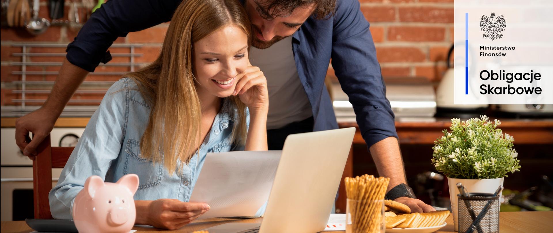 Kobieta i mężczyzna uśmiechnięci patrzą na dokument i laptopa.