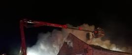 Pożar w miejscowości Brzozówka gmina Uniejów. Strażacy podają prąd wody w natarciu z podnośnika na palący się budynek. 