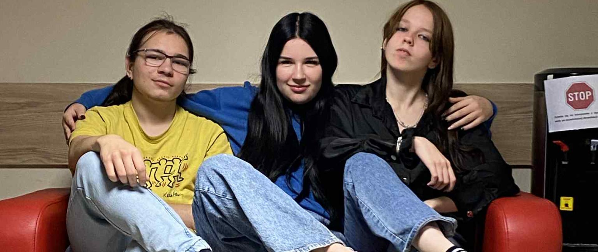 Trzy osoby siedzą na czerwonej kanapie