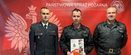 NAGRODA KOMENDANTA GŁÓWNEGO PAŃSTWOWEJ STRAŻY POŻARNEJ. Na zdjęciu trzech funkcjonariuszy podczas wręczania decyzji o przyznaniu nagrody Komendanta Głównego PSP.