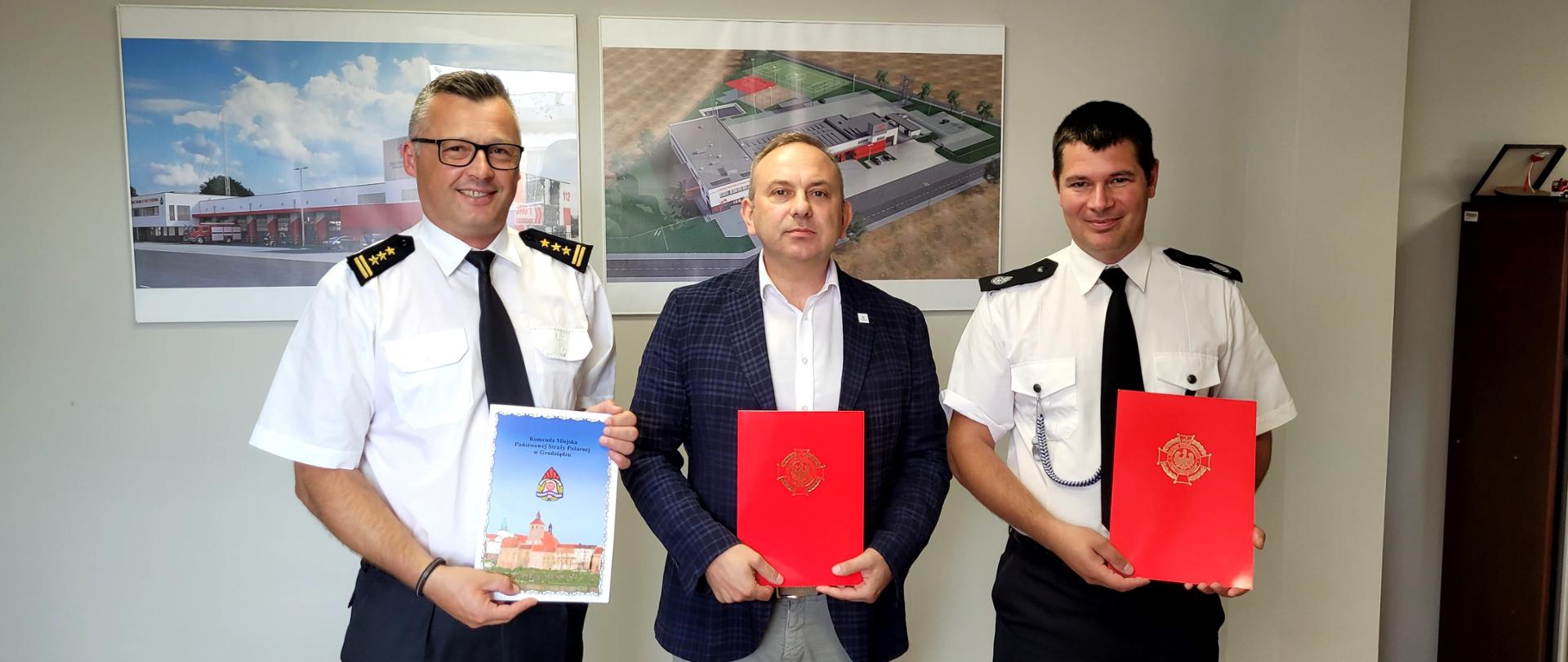 Trzej mężczyźni stojący w szeregu w jasnym pomieszczeniu. i prezentujący teczki z dokumentami.