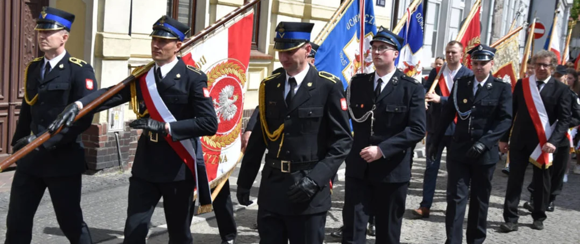 Poczty sztandarowe oraz uczestnicy maszerują ulicą na rynek.