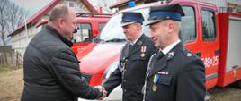 Poseł RP gratuluje dwóm druhom, którzy stoją przy strażackim samochodzie 