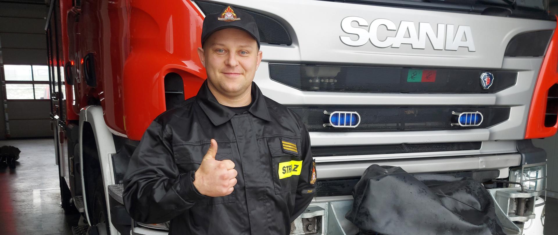 na zdjęciu widać stojącego na tle samochodu pożarniczego strażaka Tomasza Molende 